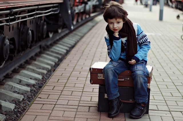 jeune garçon assis sur des valises au bord d'un quai